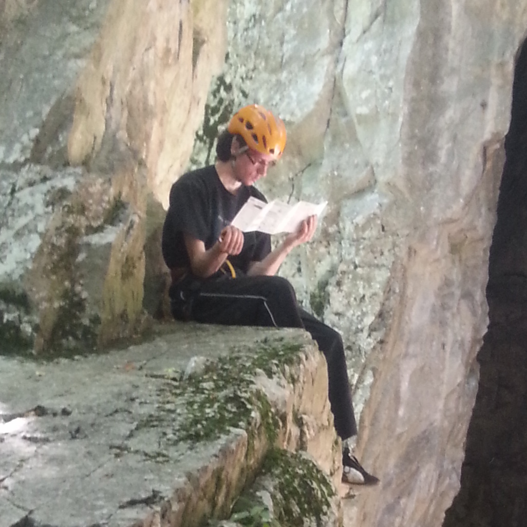 Photo of Tomas in an orange climbing helmet sitting on a rock.